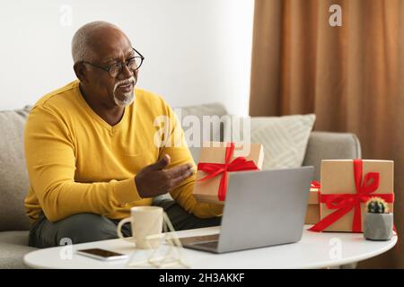 Senior Black Man Video Calling Using Laptop Showing Gift Indoor Stock Photo