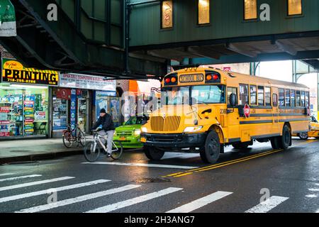 New York City, USA. Yellow schoolbus driving through the rain underneith an elevated subway track at Roosevelt Ave, Queens. Stock Photo