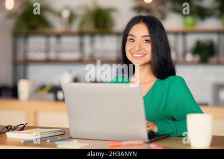 Positive millennial arabic lady looking for job online, cafe interior Stock Photo