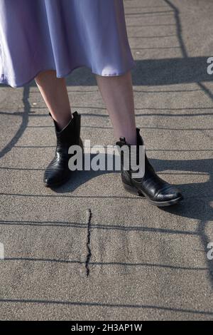 Legs of white woman in skirt and black boots on the pavement Stock Photo