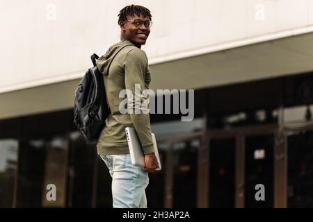Happy smiling african american student, with backpack and laptop on university background, man with mobile and work books resting on campus during lun Stock Photo