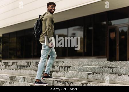 Happy smiling african american student, with backpack and laptop on university background, man with mobile and work books resting on campus during lun Stock Photo