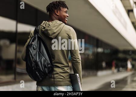 Happy smiling african american student, with backpack and laptop on university background, man with mobile and work books resting on campus during lun Stock Photo