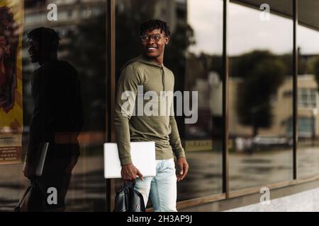 Happy smiling african american student, with backpack and laptop on university background, man with mobile and work books resting on campus during lun Stock Photo