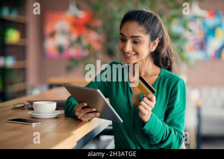 Cheerful indian lady banking online, using digital tablet at cafe Stock Photo
