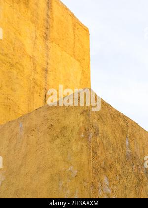 rough plastered painted yellow wall and blue sky in autumn twilight Stock Photo