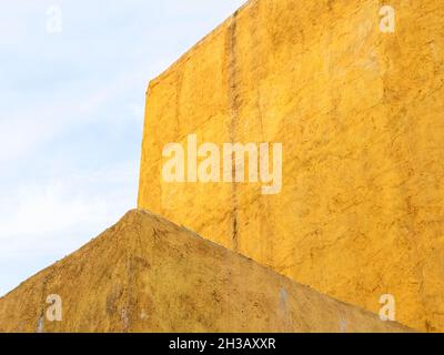 rough plastered colored yellow walls and blue sky in autumn evening Stock Photo