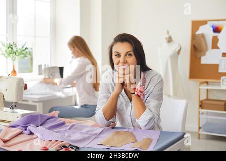 Portrait of cheerful beautiful young woman seamstress working in sewing workshop. Stock Photo