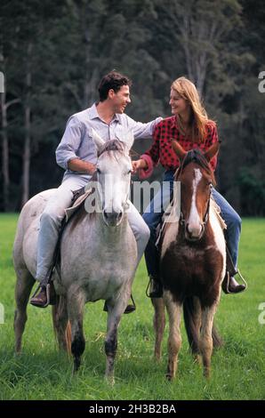 Young couple outdoors riding horses.