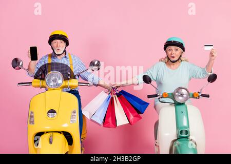 Photo of shocked married couple two mature people in helmet drive ride moped after shopping isolated on pink color background Stock Photo
