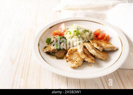 Low carb diet meal with fried chicken, cauliflower rice, mushroom ragout and tomatoes on a white plate and a light wooden table, copy space, selected Stock Photo