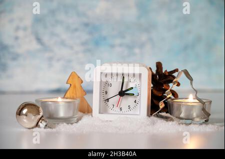 Changing to winter time, modern alarm clock showing the hour switch, artificial snow, candles an Christmas decoration against a light blue background, Stock Photo