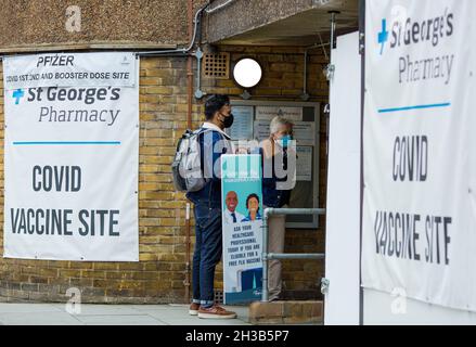 Banners of a Covid vaccine site are seen displayed outside a pharmacy as people arrive in London, 23 October 2021. Stock Photo