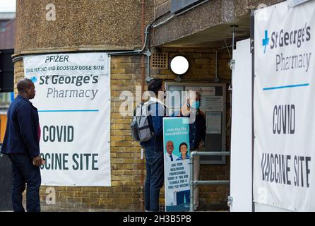 Banners of a Covid vaccine site are seen displayed outside a pharmacy as people arrive in London, 23 October 2021. Stock Photo