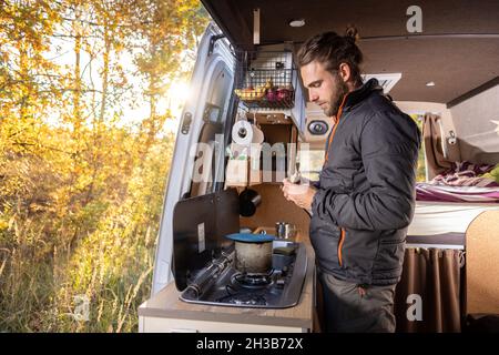 Man in the kitchen area of his camper van in autumn Stock Photo