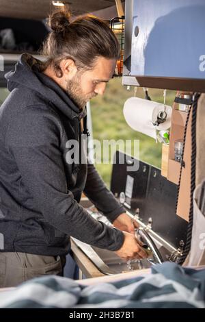 Man washing the dishes inside a caravan Stock Photo