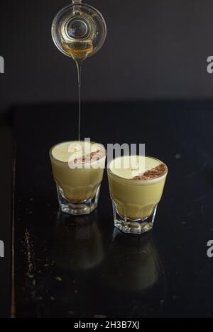 Two elegant glasses of golden milk in gibraltar glasses topped with cinnamon while barista drizzles cinnamon on top. Stock Photo