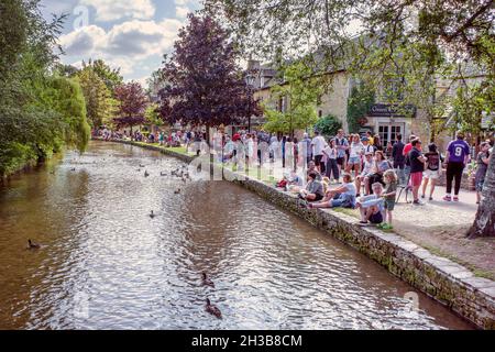 Visitors to Bourton On The Water line the bank of the River Windrush. The Cotswolds, United Kingdom. Stock Photo