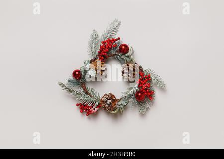 Christmas artificial wreath from branches of evergreen trees with cones and berries on an isolated light gray background. Stock Photo