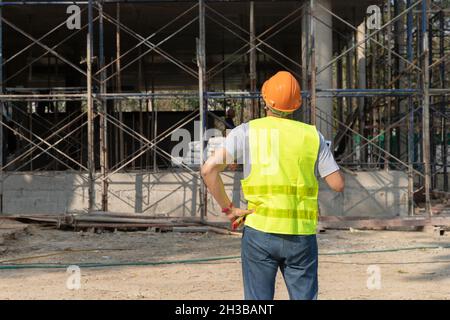 Rear view of engineer or contractor standing at a building site. Young businessman construction site engineer. Stock Photo