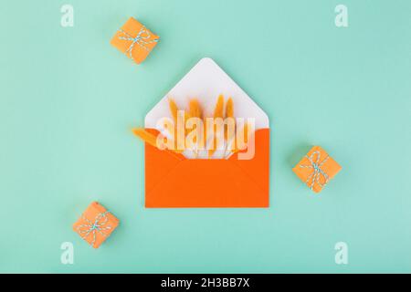 Orange envelope and dry flowers, lagurus, with copy space, on blue table with small gifts. Season gift-giving concept Stock Photo