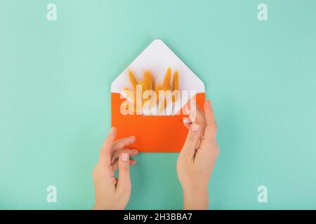 Orange envelope and dry flowers, lagurus, with woman hands, on blue table.  Stock Photo