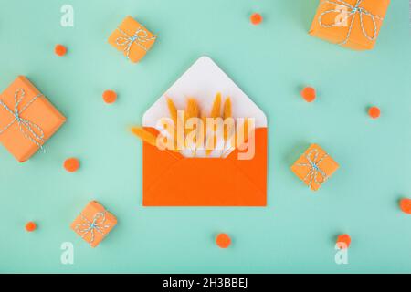 Orange envelope and dry flowers, lagurus, with copy space, on blue table with small gifts. Season gift-giving concept Stock Photo