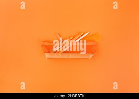 Different orange school supplies in case on orange table. Back to school concept. Flat lay, top view. Orange rush. Stock Photo