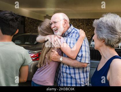 Smiling grandfather hugs teen granddaughter as grandmother looks on. Stock Photo