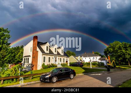 Phenomenal double rainbow glowing above home under a dramatic sky. Stock Photo