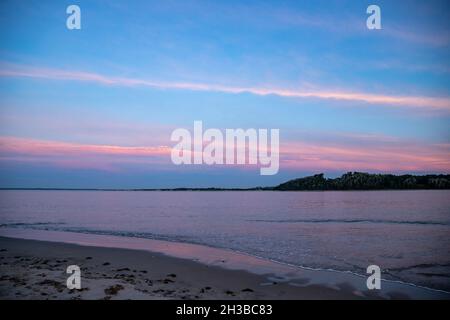 Colorful clouds reflecting on the ocean shoreline during sunset. Stock Photo