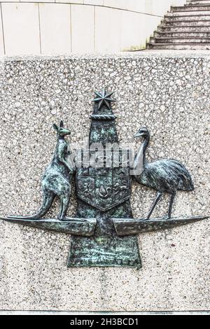 Australian Commonwealth Coat of Arms upheld by native fauna kangaroo and emu depicted in grungy metal on rough rock surface with walls and steps in ba Stock Photo