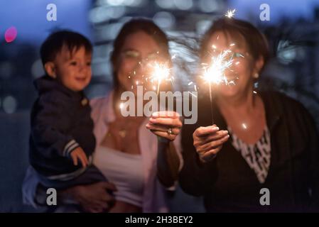 Latino Mother Grandmother and baby boy celebrating christmas new year holidays having fun with sparklers at dawn. Stock Photo