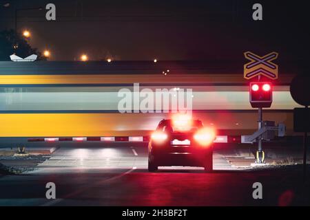 Railway at night. Passenger train passing by railroad crossing while red warning lights stopped car Stock Photo