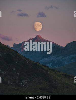 Moon rising during sunset aligned with mountain peak top, Pyrenees. Stock Photo