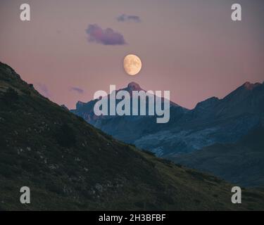 Moon rising during sunset aligned with mountain peak top, Pyrenees. Stock Photo