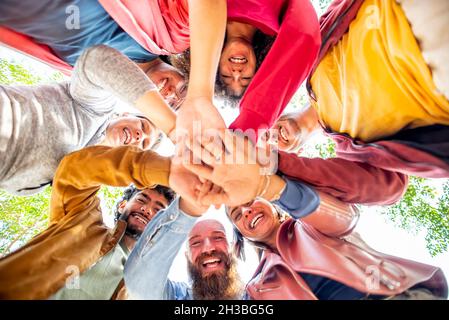 directly below portrait of happy diverse large group of multicultural friends holding hands making high five stacking them together outdoors. Stock Photo