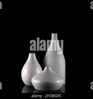 Three curvy white vases on black, with reflection. Stock Photo
