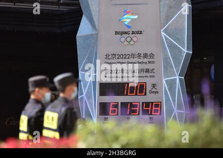 Beijing, China. 27th Oct, 2021. Two security guards walk past the countdown board for the opening of the Winter Olympic Games in Wangfujing Street.Today the Beijing 2022 Winter Olympic Games ushered in a countdown of 100 days. On February 4, 2022, the 24th Winter Olympic Games will start in Beijing. From the 2008 Olympic Games to the upcoming 2022 Winter Olympic Games, Beijing will become the first 'double Olympic city' in Olympic history. Credit: SOPA Images Limited/Alamy Live News Stock Photo