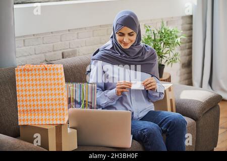 Pretty Muslim woman sitting on a couch and buying something online Stock Photo
