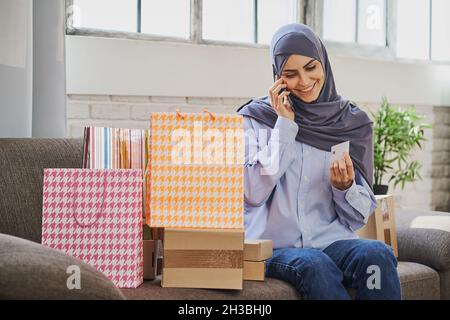 Pretty Arabian woman talking on the phone and looking at a credit card Stock Photo