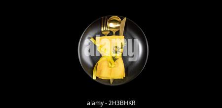 Xmas table setting banner with golden cutlery set on round black plate in center of black. Stock Photo