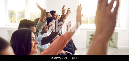 Diverse audience raising up their hands to ask speaker question after presentation Stock Photo