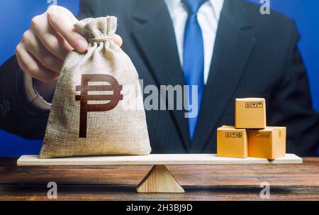 Philippine peso money bag and a bunch of boxes on scales. Trade exchange balance. Import and export, economic processes. Manufacturing, retail distrib Stock Photo