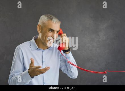 Happy smiling retired senior man talking to someone on red retro landline telephone Stock Photo