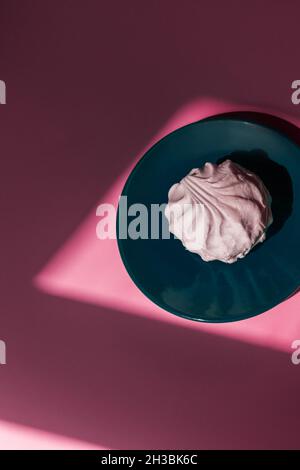One marshmallow lies on an aqua saucer on a pink background.  Stock Photo