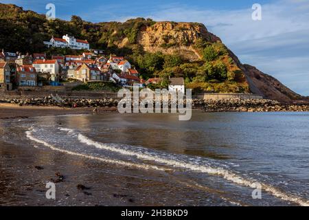 The steeply raked white-painted cottages of Runswick Bay at low-tide in the North York Moors National Park, Yorkshire, England Stock Photo