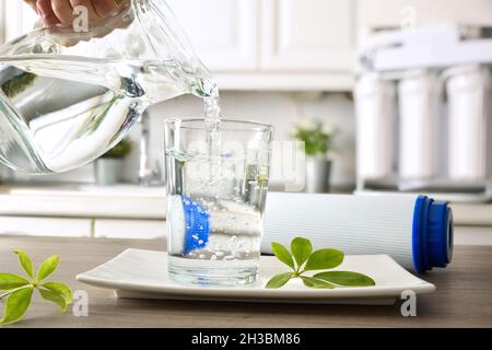 Hand filling crystal glass on kitchen bench from jug with filtered water using reverse osmosis household equipment. Front view. Horizontal composition Stock Photo