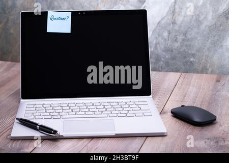 The photo shows a notebook on a wooden table, on the display is stuck the message questions Stock Photo