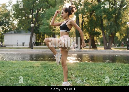 Side view shot of fit young woman doing cardio interval workout in the park at sunrise. Fitness woman working out outdoors in the morning. Stock Photo